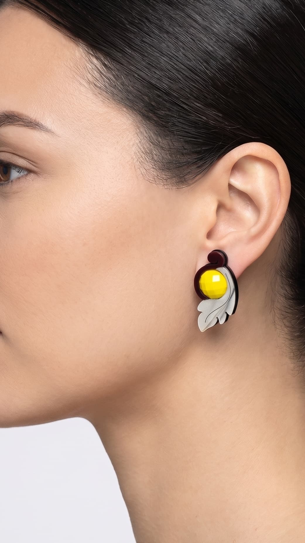 modelo de perfil luciendo uno de los pendientes de acrílico de Gissa Bicalho, mostrando su proporción y cómo se asienta elegantemente sobre el lóbulo de la oreja.
