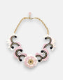 plano frontal del collar maximalista de Gissa Bicalho sobre fondo neutro, mostrando la composición de acrílico de alta calidad con una flor central, volutas ornamentales y su cadena dorada con cierre.