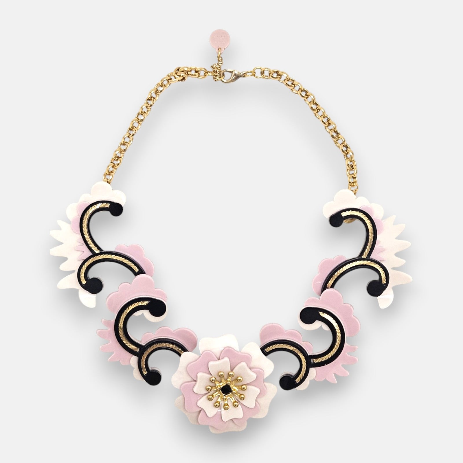 plano frontal del collar maximalista de Gissa Bicalho sobre fondo neutro, mostrando la composición de acrílico de alta calidad con una flor central, volutas ornamentales y su cadena dorada con cierre.