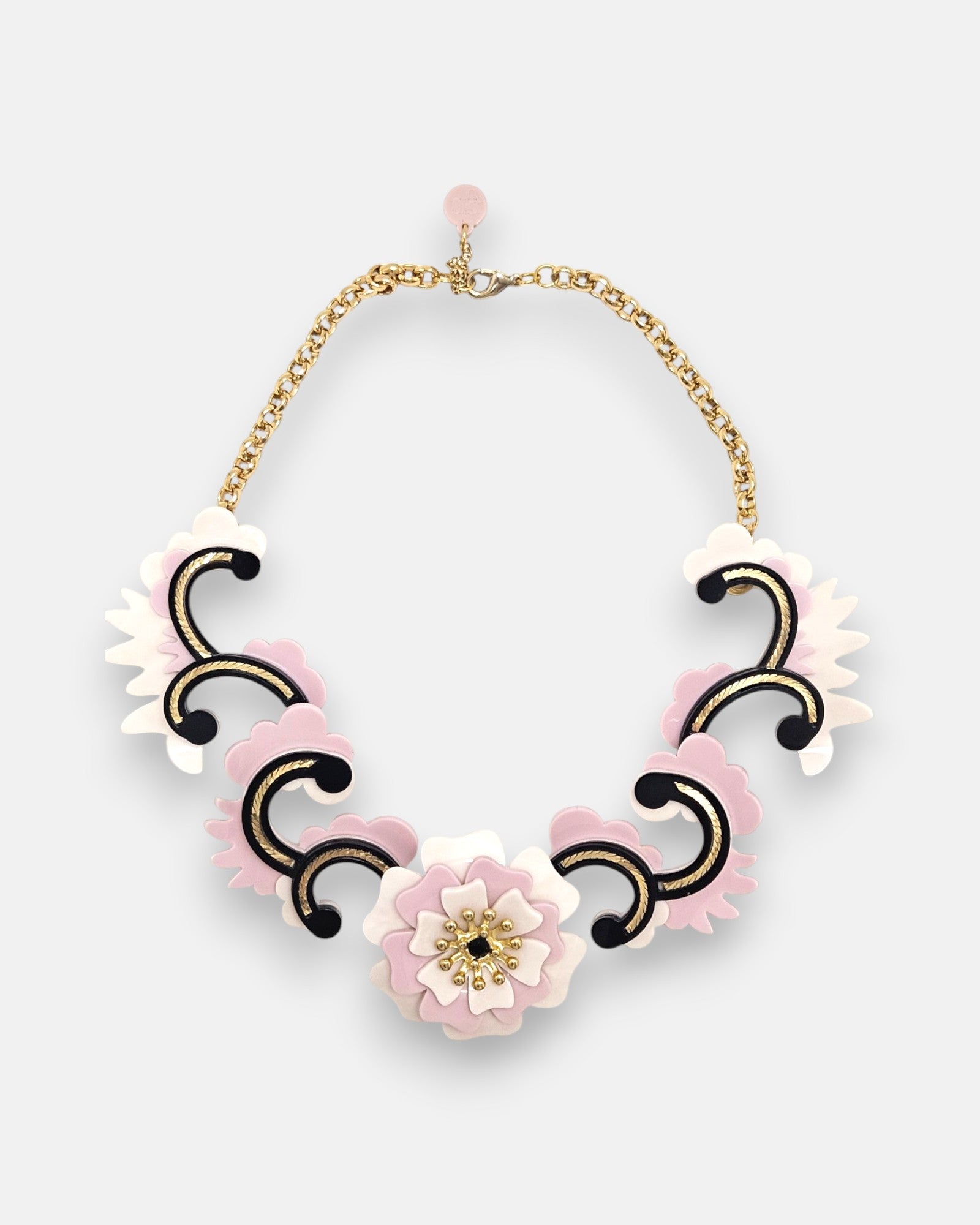 plano frontal del collar maximalista de Gissa Bicalho sobre fondo neutro, mostrando la composición de acrílico de alta calidad con una flor central, volutas ornamentales y su cadena dorada con cierre.