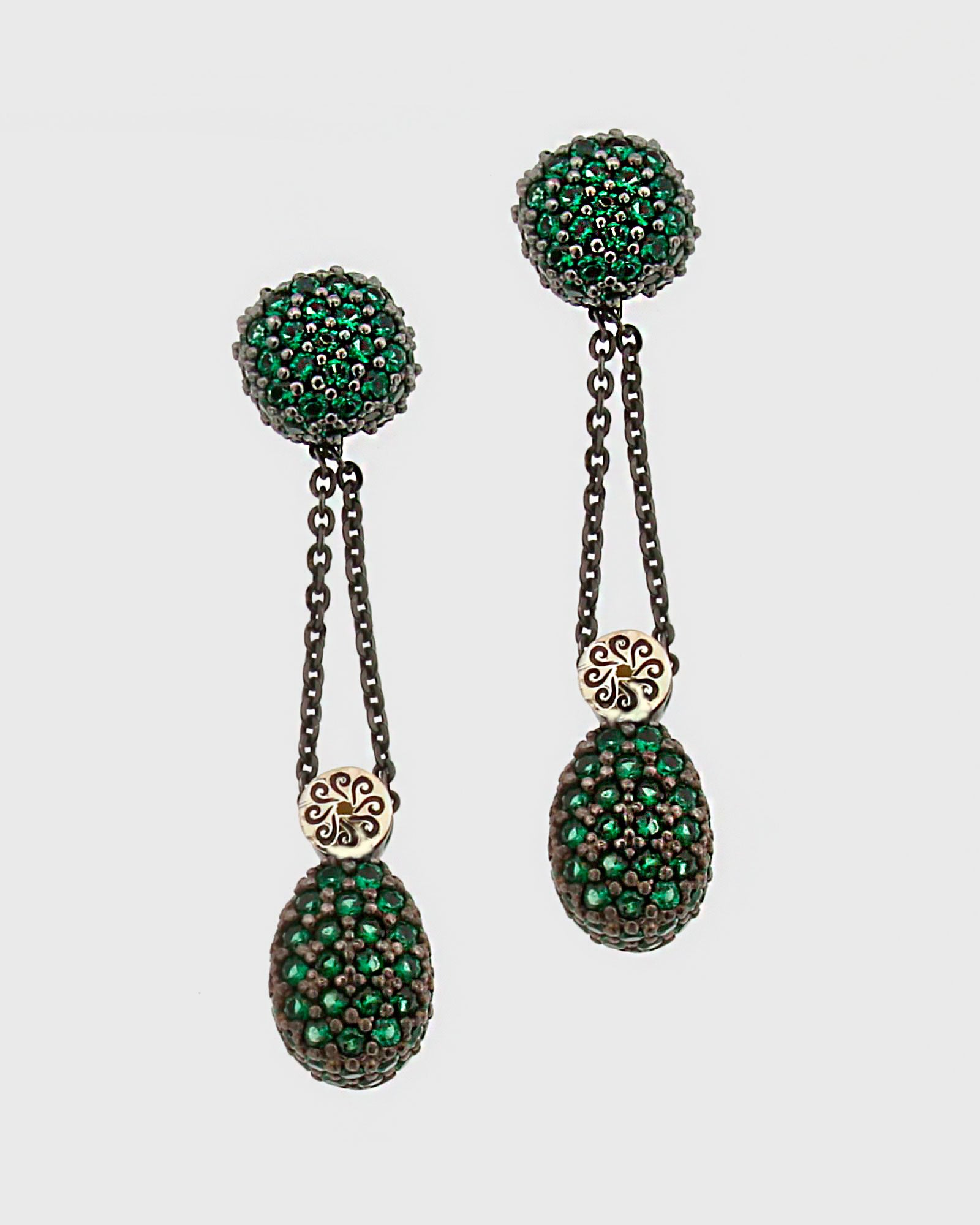 Pareja de pendientes largos Bohemme con esferas de circonitas verdes y cadenas de plata oxidada sobre fondo blanco.