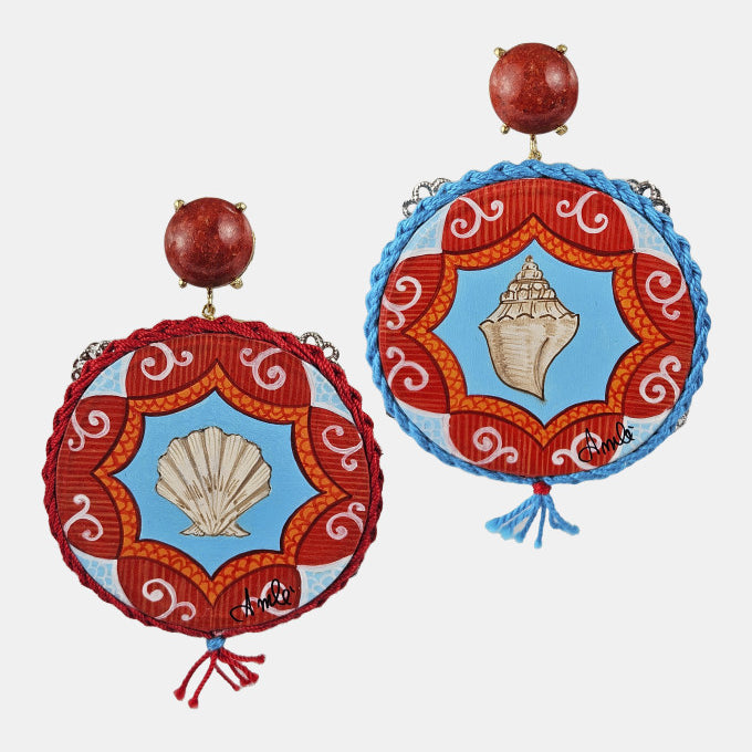 Pareja de pendientes Amlé tipo pandereta pintados a mano con conchas marinas y detalles de coral rojo sobre fondo gris claro.