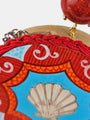 Detalle del acabado artesanal del pendiente Amlé mostrando el trenzado de algodón rojo, la pintura sobre madera y la esfera de coral.