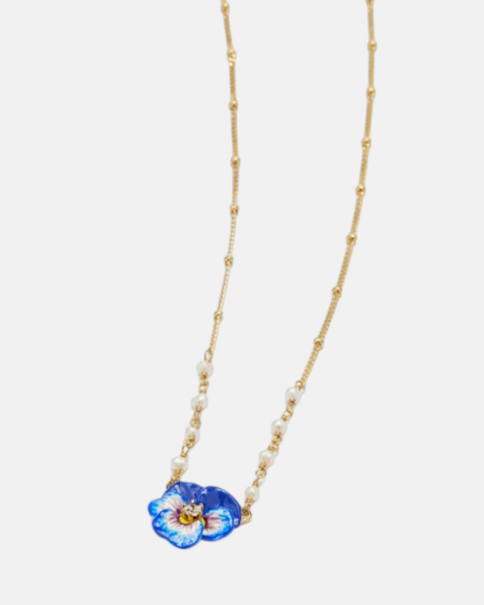 Primer plano del colgante floral Les Néréides con flor pensamiento esmaltada a mano en tonos azul y violeta con cristal central.