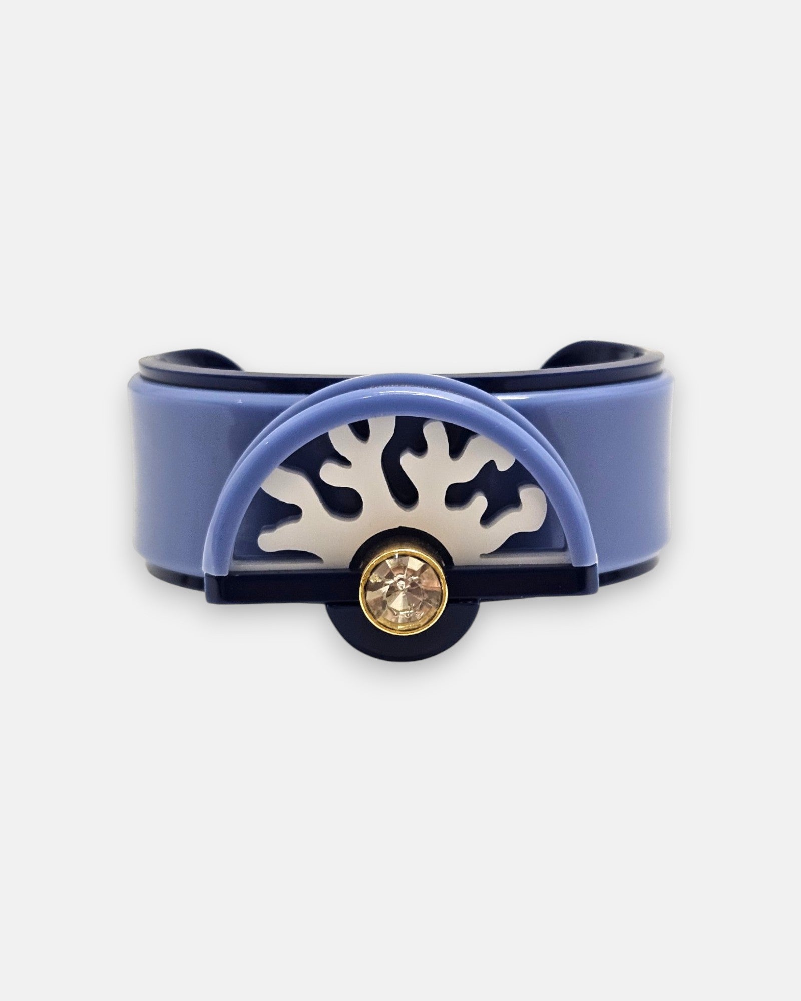vista frontal del brazalete rígido de Gissa Bicalho realizado en acrílico de alta calidad con un aplique semicircular de diseño de coral y un cristal redondo brillante en el centro.