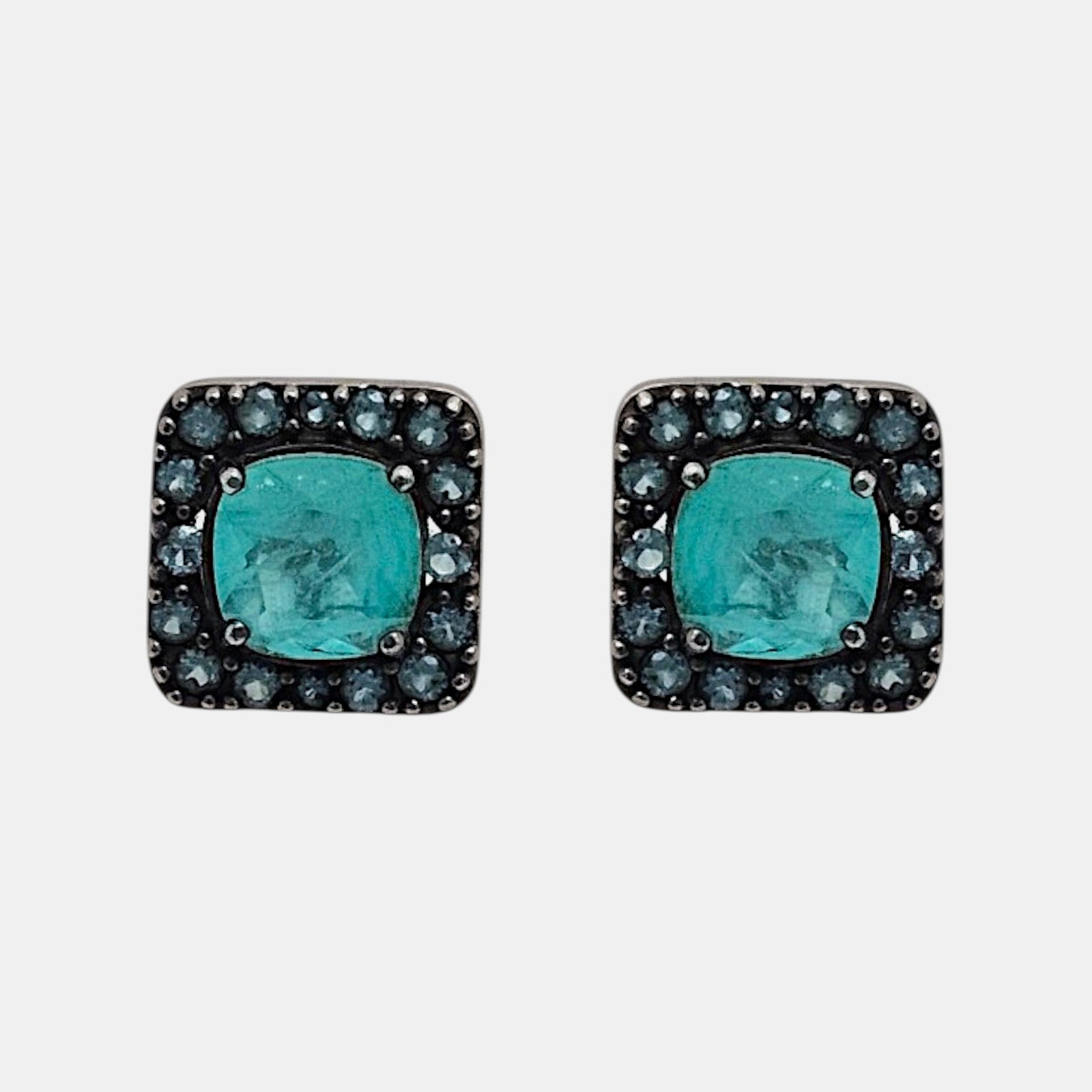 Pareja de pendientes de botón cuadrados Bohemme con piedra turquesa central y orla de circonitas azules sobre plata oxidada.