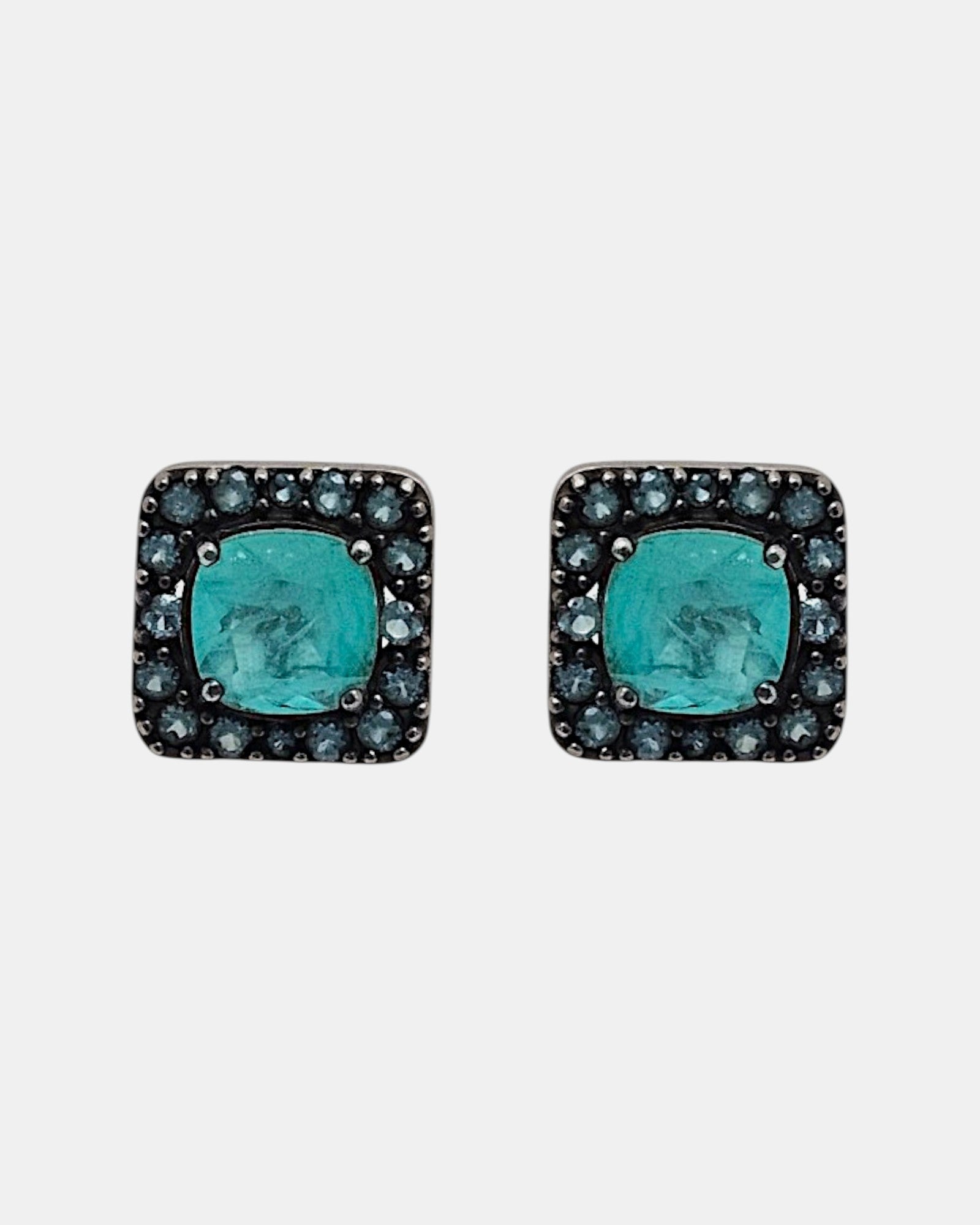 Pareja de pendientes de botón cuadrados Bohemme con piedra turquesa central y orla de circonitas azules sobre plata oxidada.