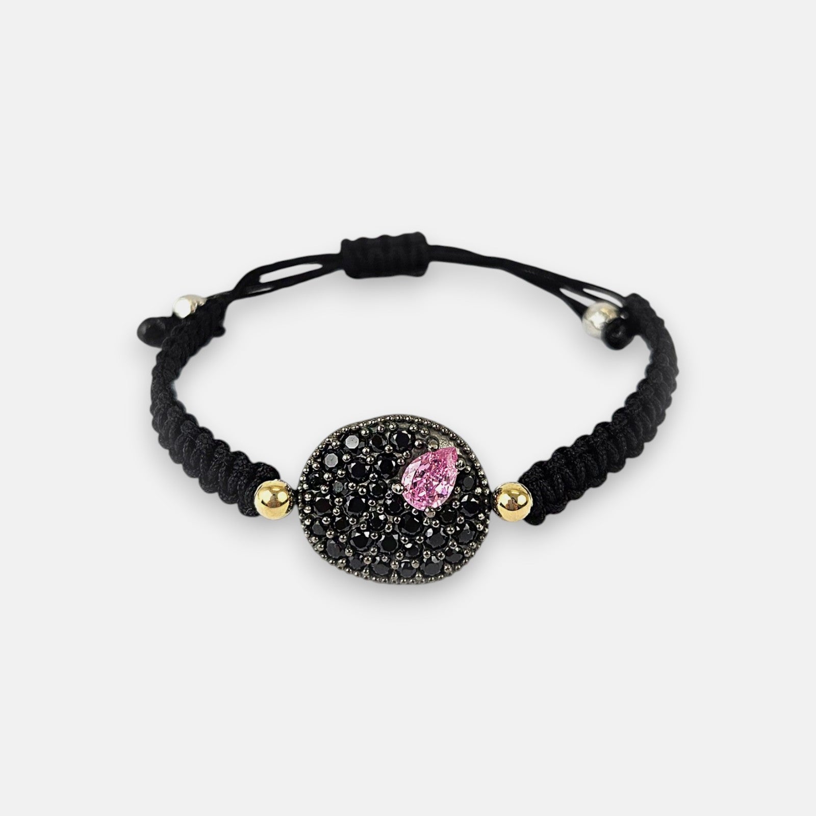 Pulsera de cordón negro Bohemme con medallón circular de espinelas negras y piedra central rosa.