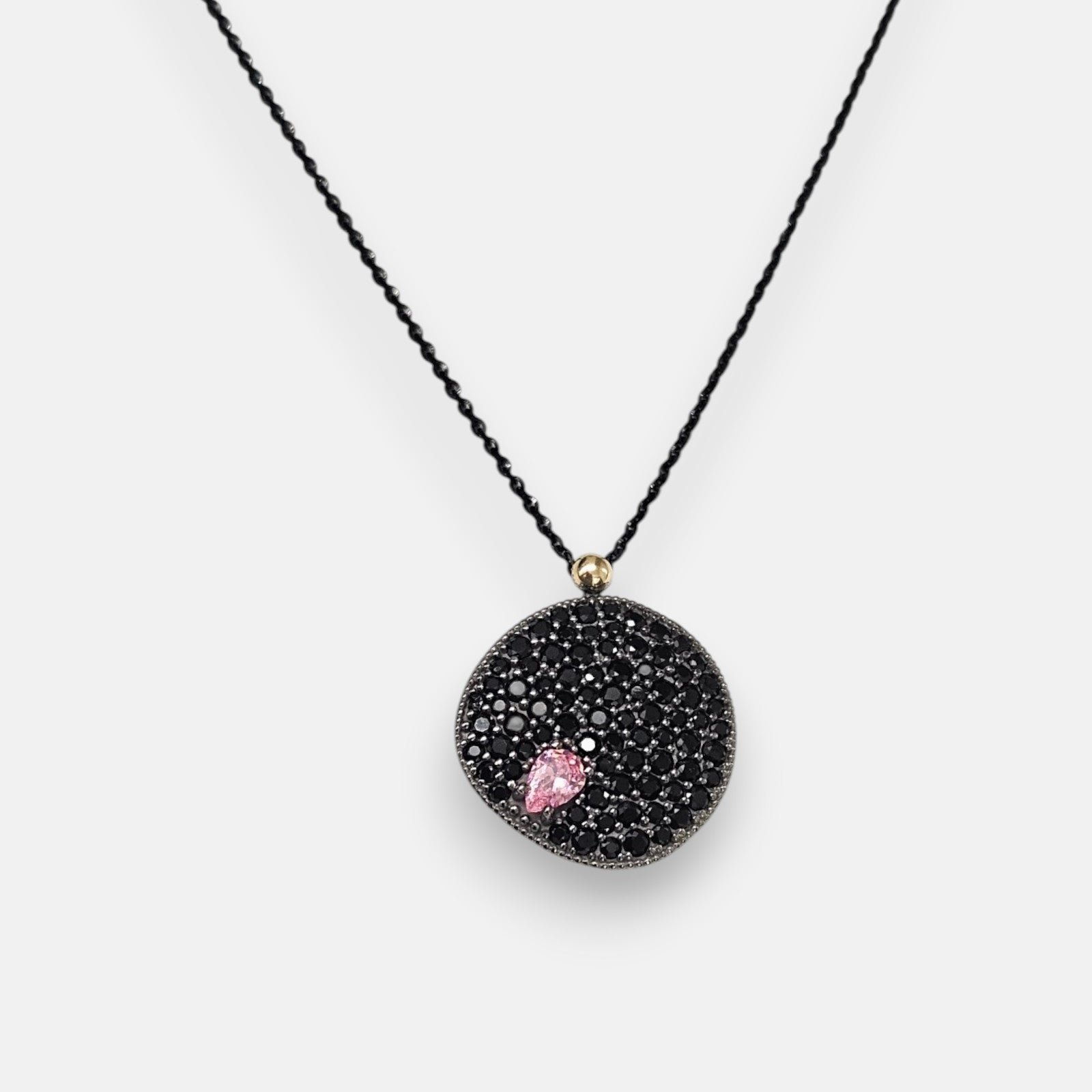 Colgante circular Bohemme con medalla de espinelas negras y detalle de piedra rosa sobre cadena negra.