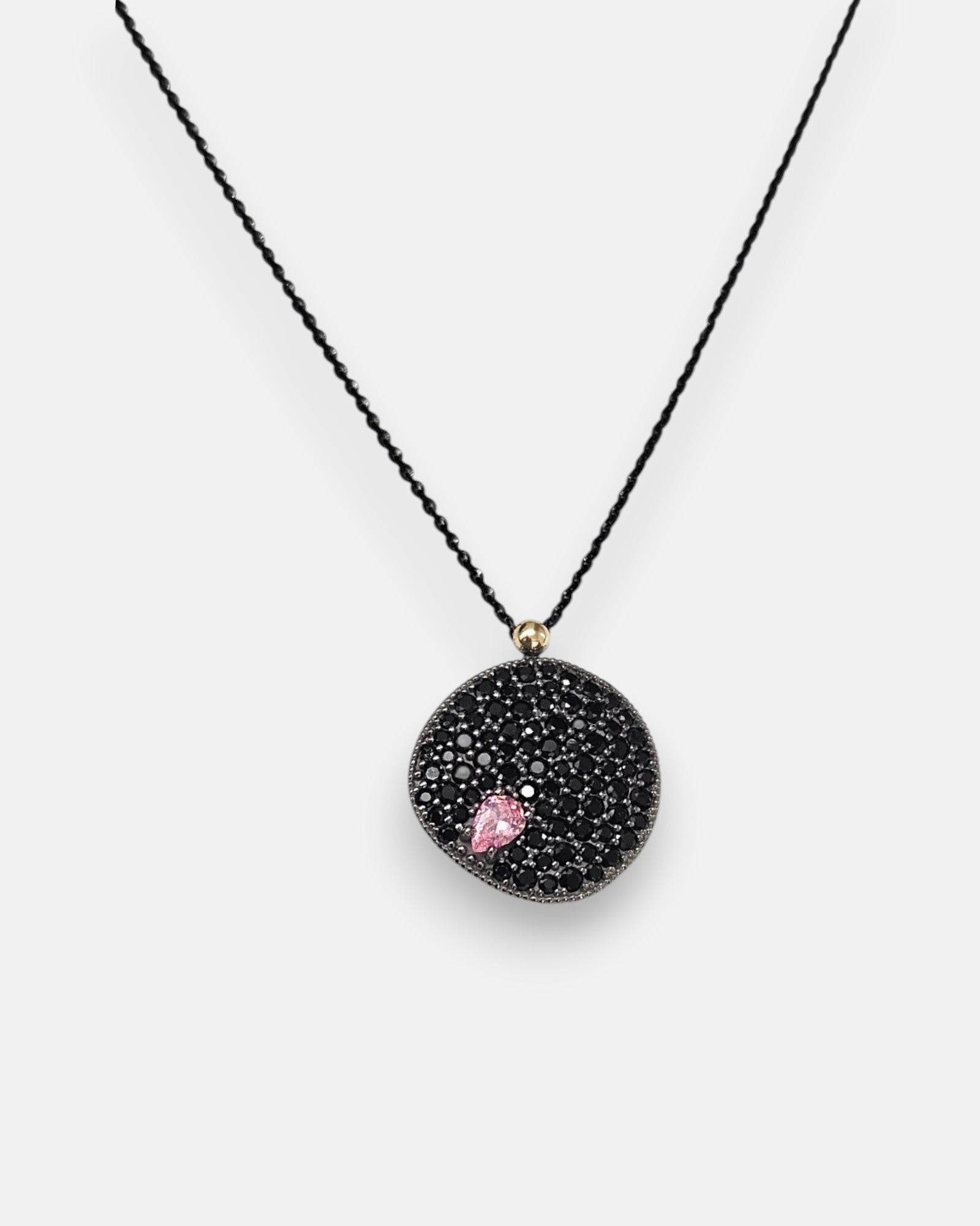 Colgante circular Bohemme con medalla de espinelas negras y detalle de piedra rosa sobre cadena negra.
