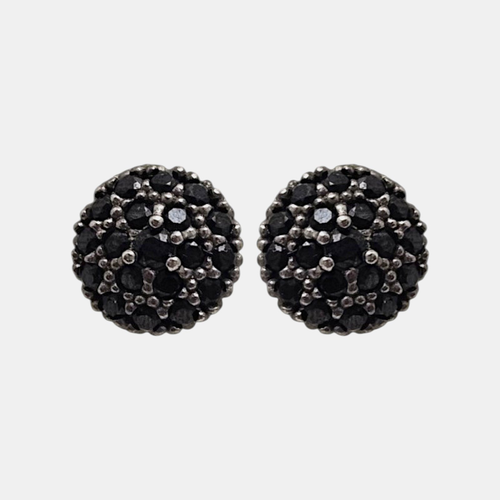 Pareja de pendientes de botón circulares Bohemme con pavé de espinelas negras sobre fondo gris claro.