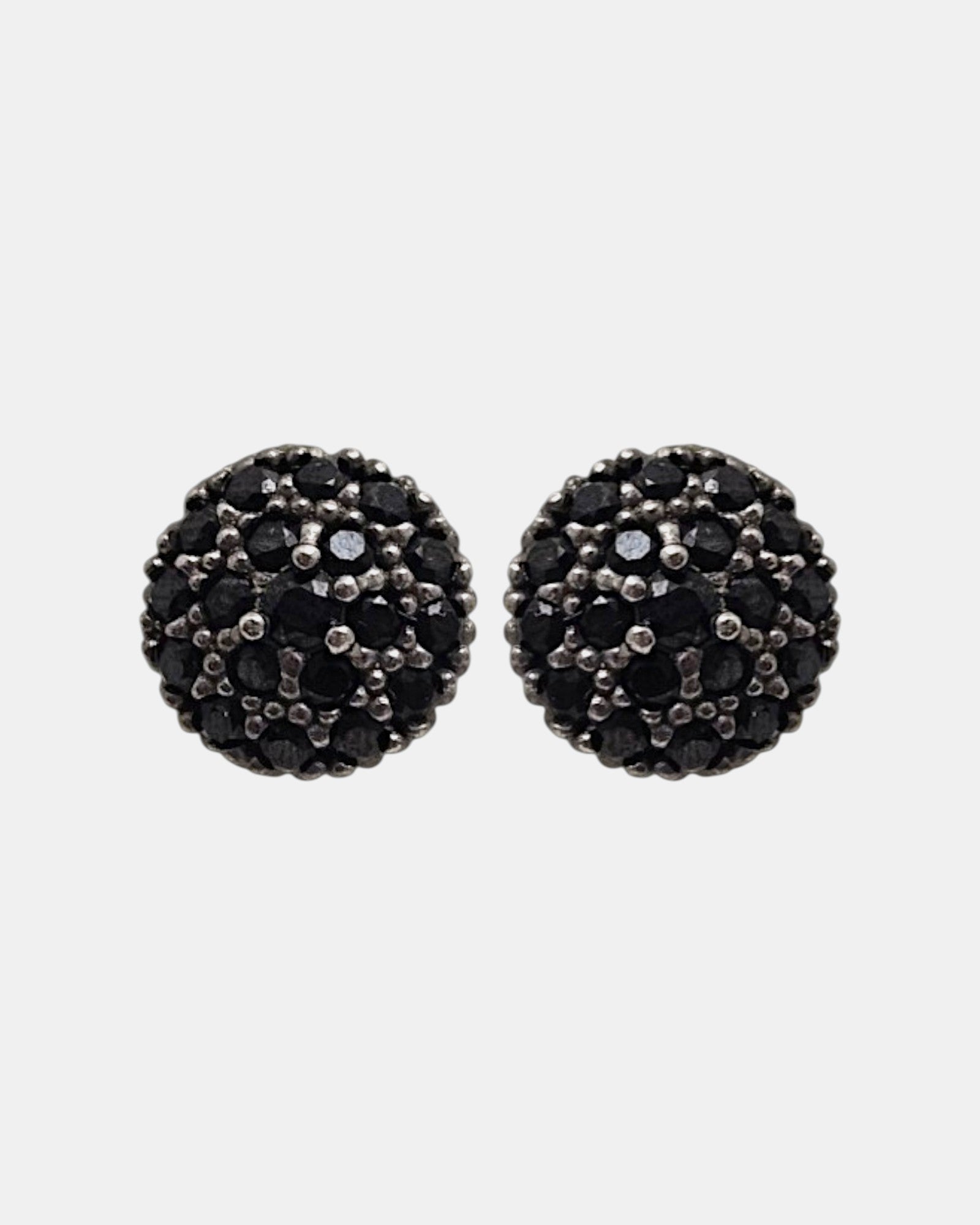 Pareja de pendientes de botón circulares Bohemme con pavé de espinelas negras sobre fondo gris claro.