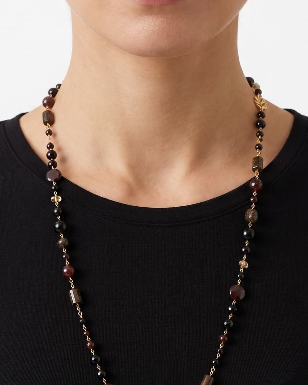 Primer plano de mujer luciendo el collar largo Amlé, resaltando el diseño elegante y los tonos tierra sobre un top negro.