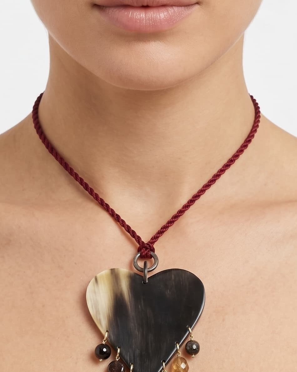 Mujer luciendo el collar de corazón de cuerno Amlé, resaltando su caída y el contraste del cordón burdeos sobre su piel.