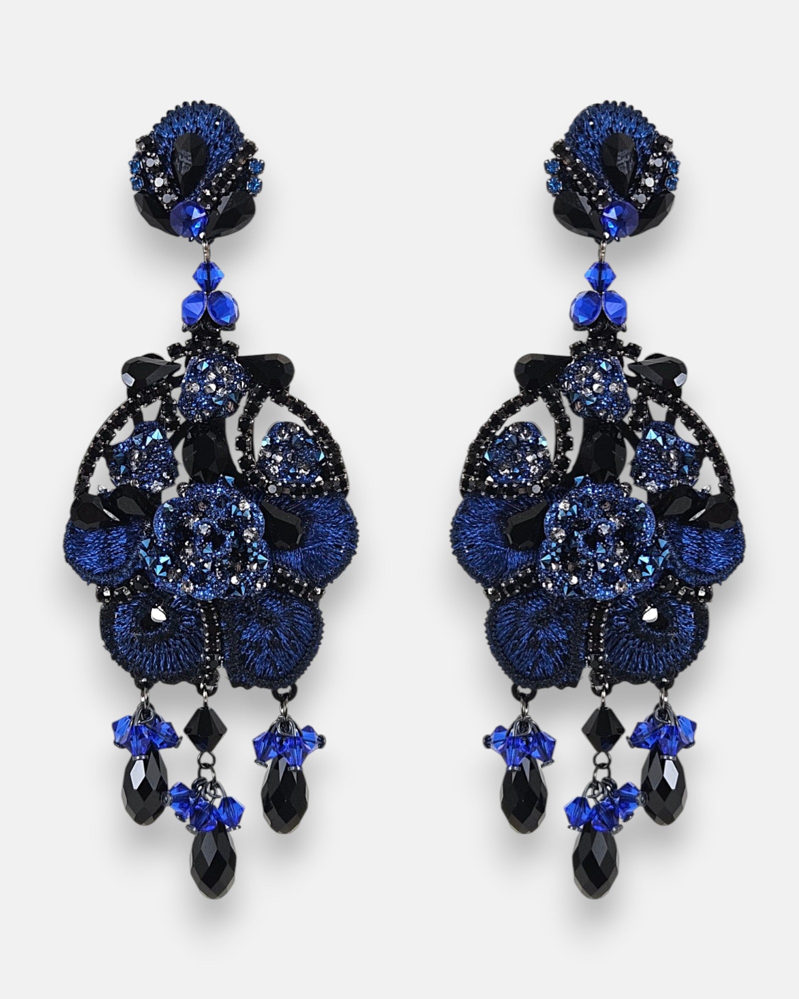 Pareja de pendientes maxi Dublos con flor de seda bordada en azul cobalto y detalles de cristales negros sobre fondo gris claro.