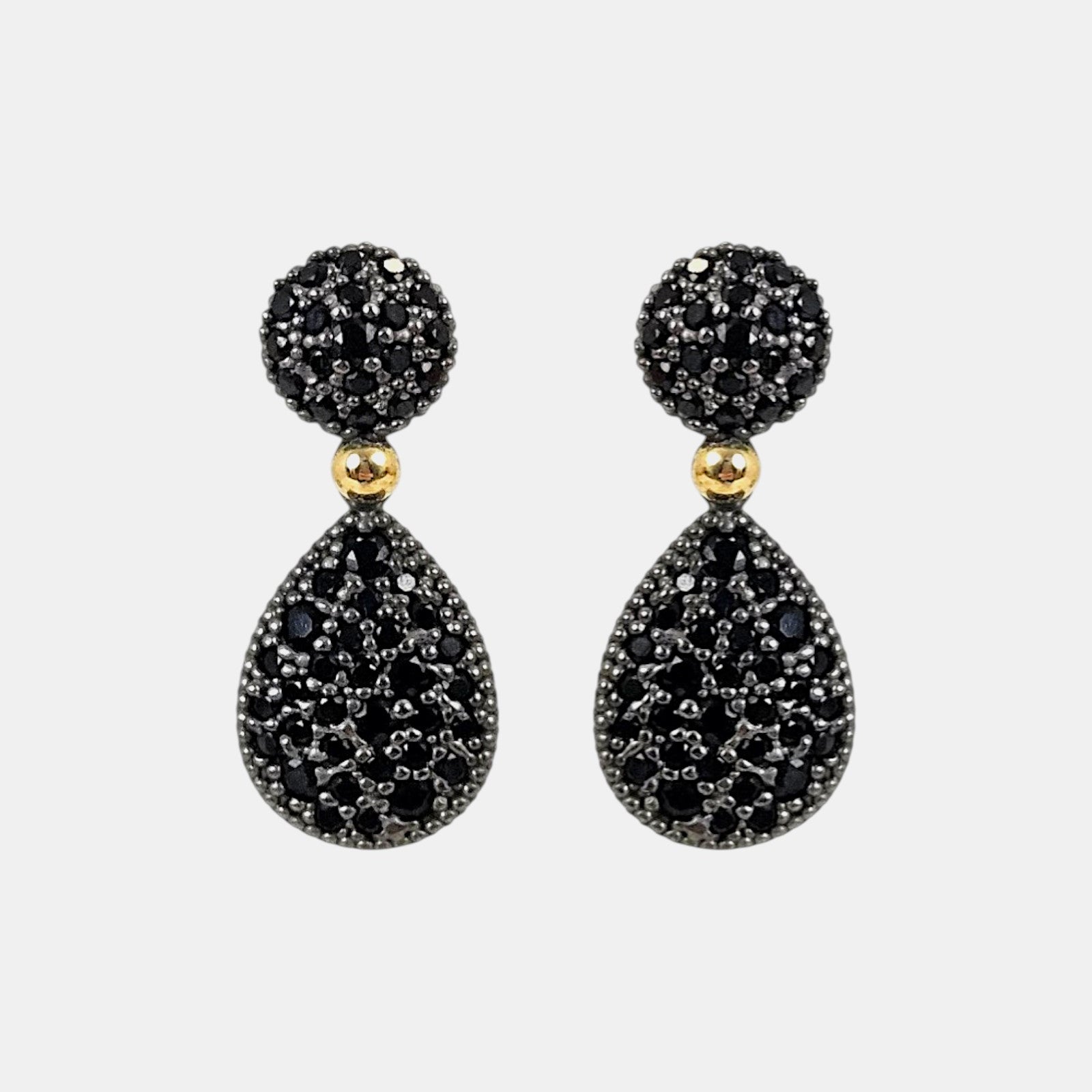 Pareja de pendientes articulados Bohemme con botón y lágrima en pavé de espinelas negras sobre fondo gris claro.