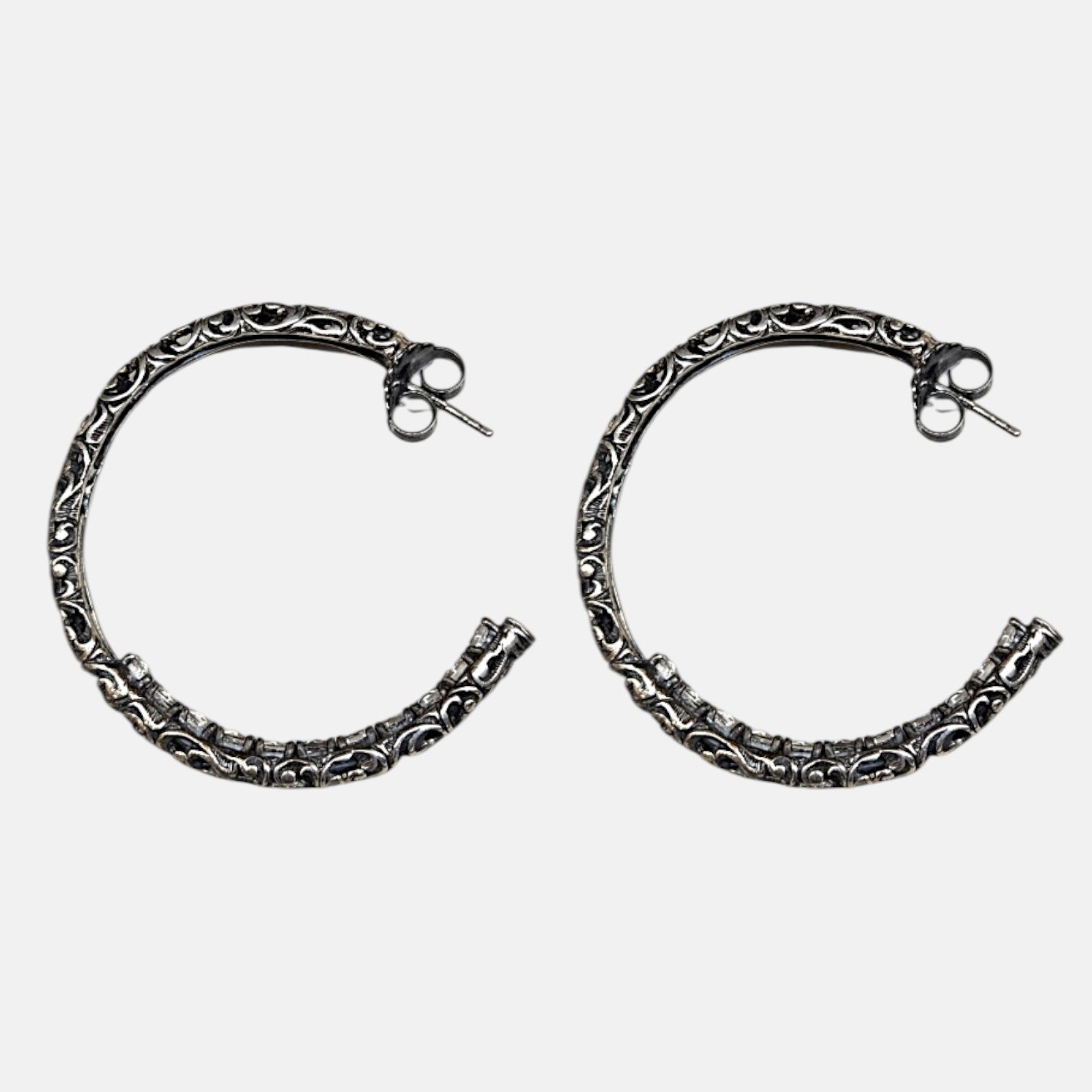Pendientes de aro en plata de ley envejecida con
grabado calado artesanal de la marca Sanci sobre fondo gris claro.