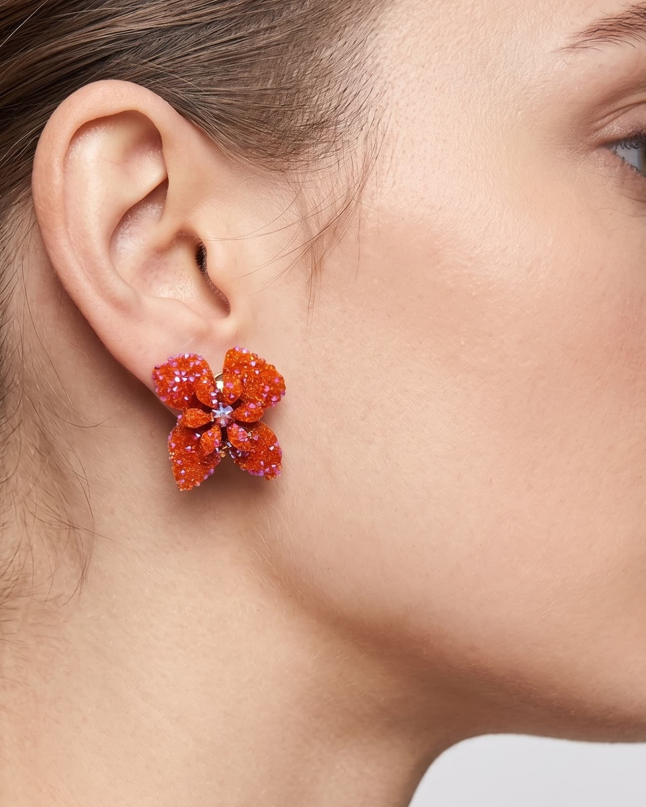 Vista de un pendiente de botón Flor de Neroli naranja colocado en una modelo, mostrando su tamaño compacto y cómo queda pegado al lóbulo.