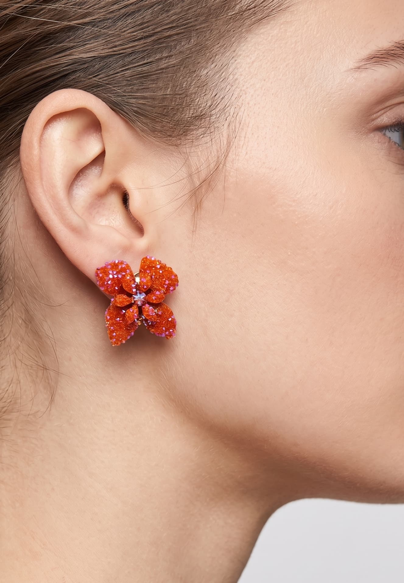 Vista de un pendiente de botón Flor de Neroli naranja colocado en una modelo, mostrando su tamaño compacto y cómo queda pegado al lóbulo.