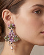  modelo luciendo el Pendiente Cruz Floral Malva de Dublos, apreciando la escala, el enmarque sobre el rostro y las lágrimas colgantes.   