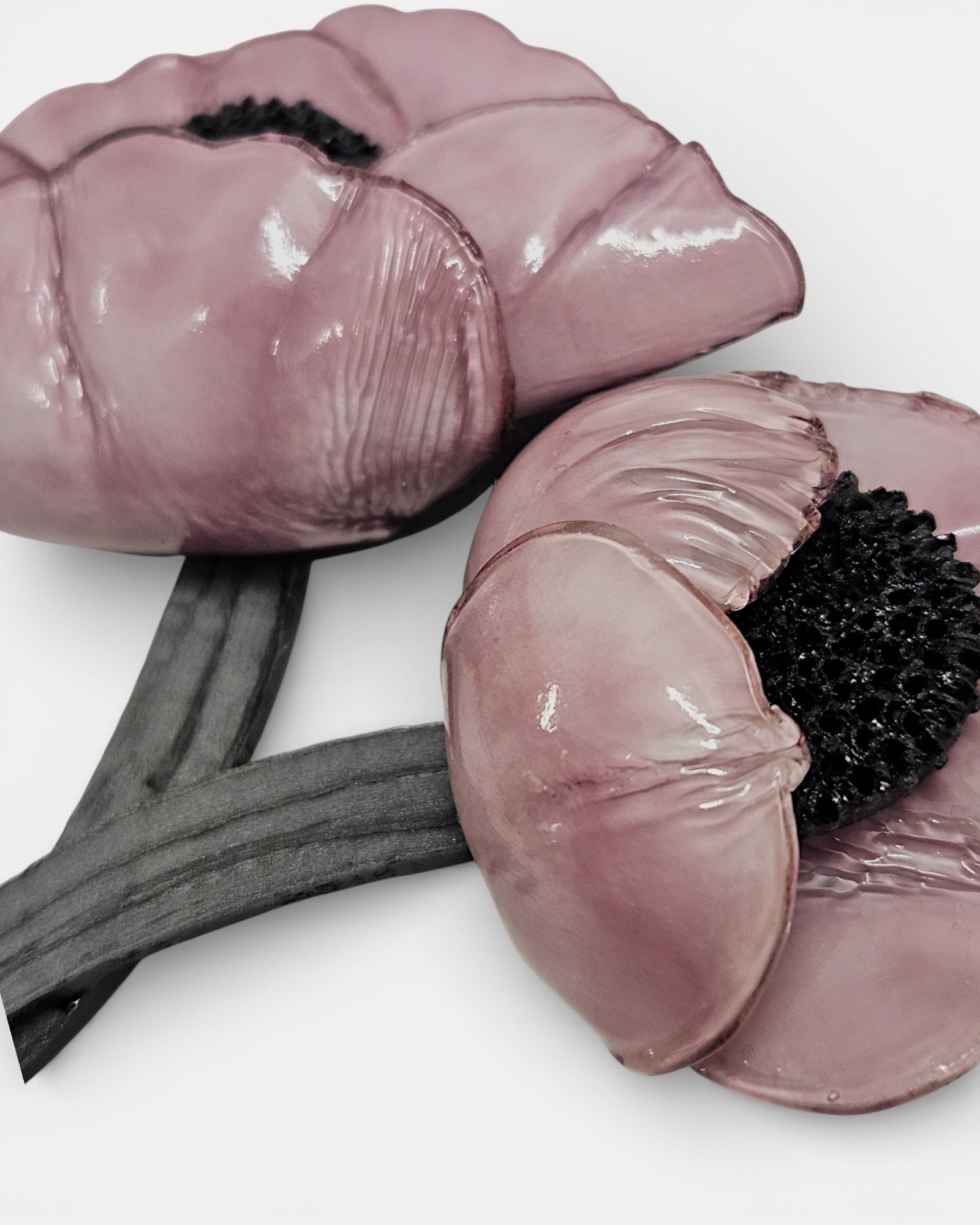 Broche artesanal de dos amapolas color rosa empolvado sobre chaqueta azul" y "Primer plano de broche floral rosa con acabado brillante y centro negro".