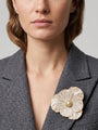 Vista en ángulo del maxibroche floral crema y oro de Ciléa Paris prendido en una chaqueta de tweed gris, detallando su volumen tridimensional sobre la solapa.