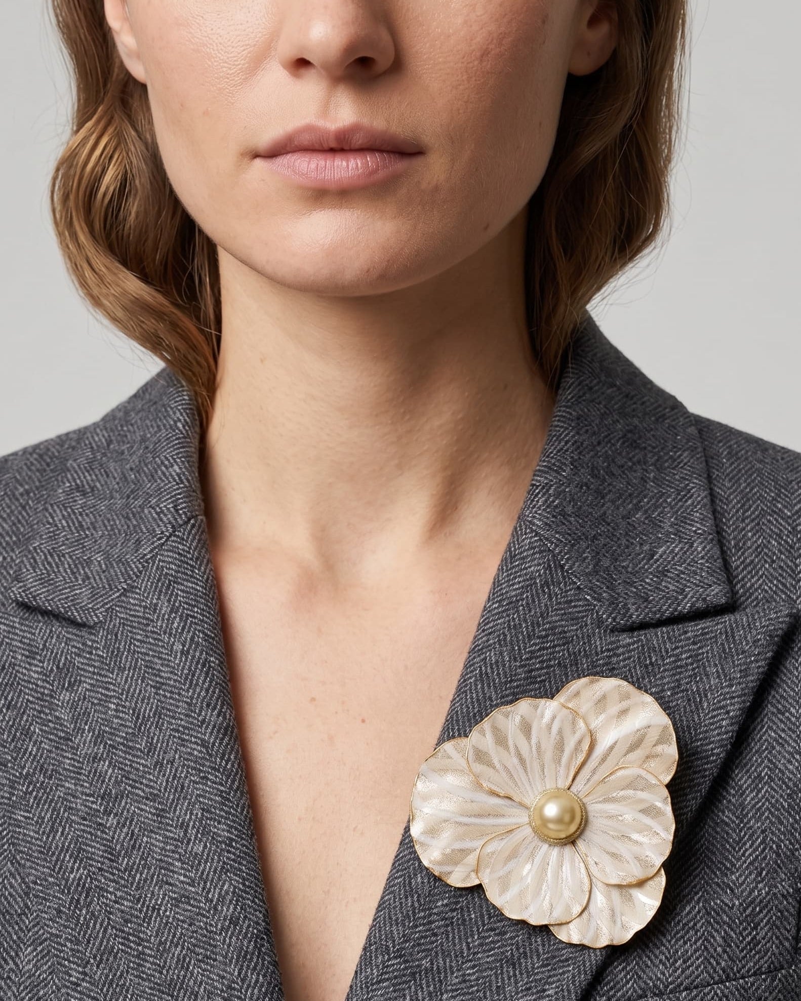 Vista en ángulo del maxibroche floral crema y oro de Ciléa Paris prendido en una chaqueta de tweed gris, detallando su volumen tridimensional sobre la solapa.