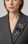 Vista lateral del maxibroche floral negro de Ciléa Paris prendido en una chaqueta de lana gris, detallando su silueta estilizada con tallo sobre la solapa.