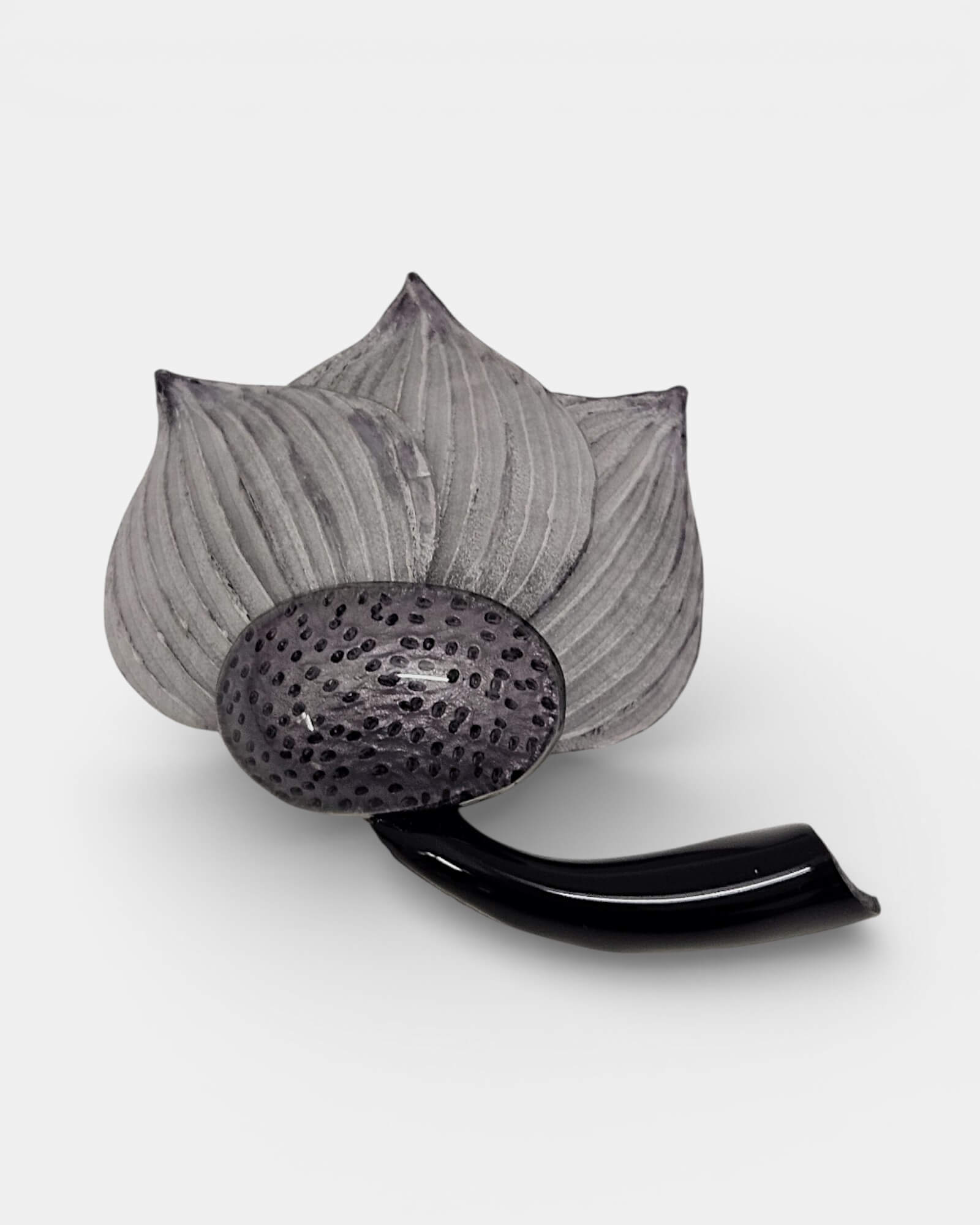 "Broche de diseño contemporáneo con forma de loto gris y negro, colocado en la solapa de una prenda verde. Joyería de autor con acabados mate y brillante."