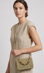 modelo vistiendo un vestido de lino beige de perfil mientras luce el bolso verde de Emanuela Caruso colgado al hombro mediante su fina correa de cadena dorada.