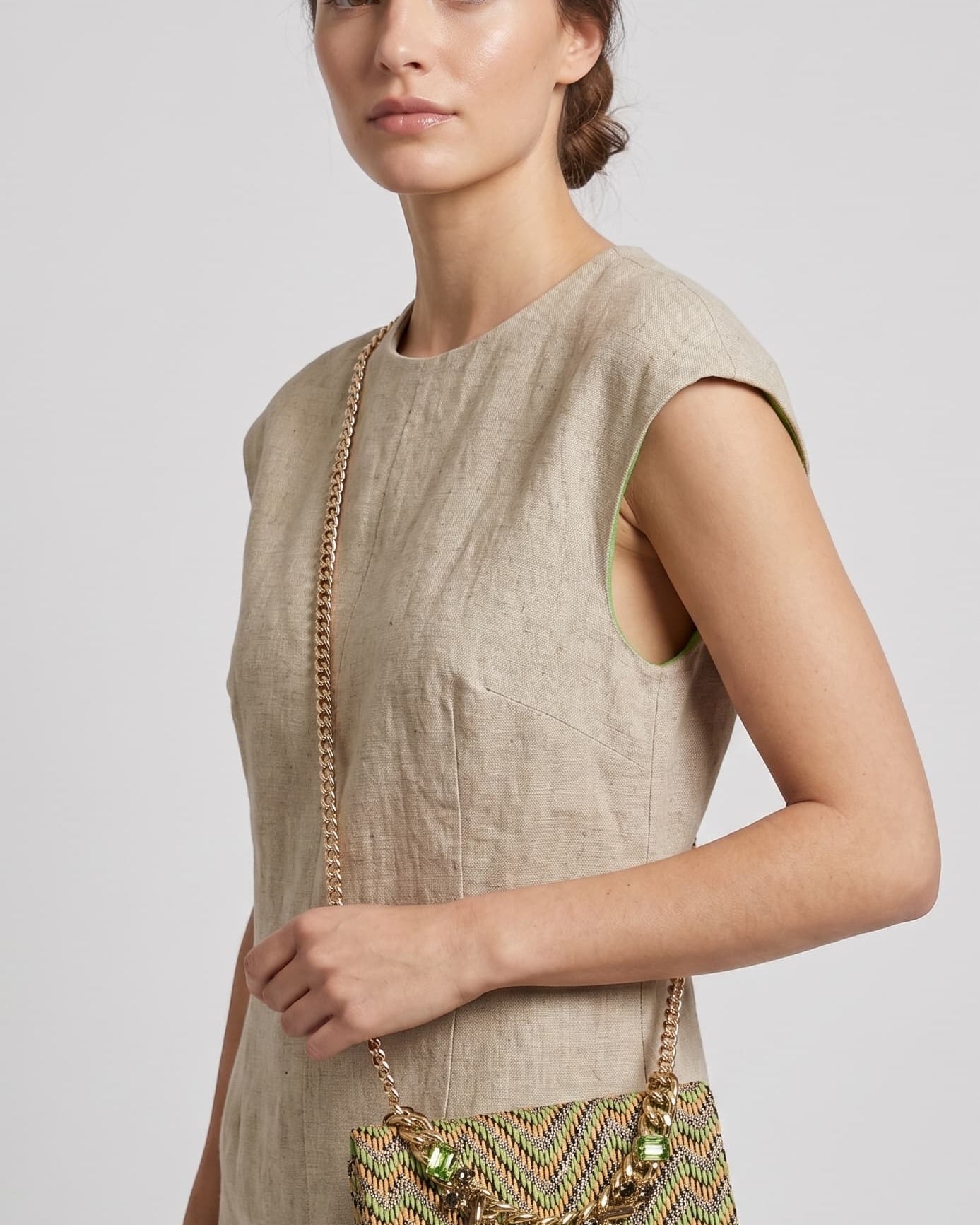 modelo vistiendo un vestido de lino beige de perfil mientras luce el bolso verde de Emanuela Caruso colgado al hombro mediante su fina correa de cadena dorada.