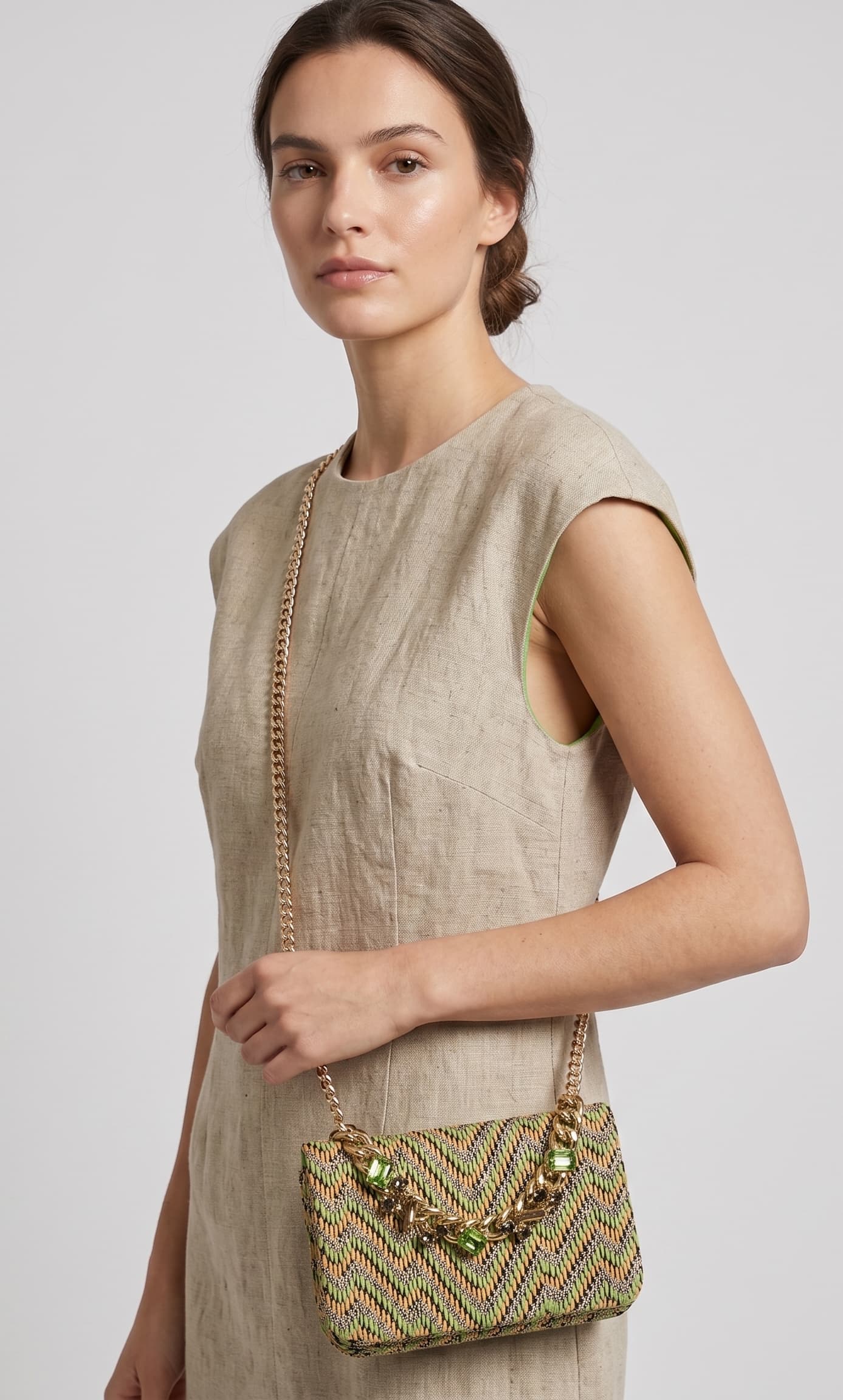 modelo vistiendo un vestido de lino beige de perfil mientras luce el bolso verde de Emanuela Caruso colgado al hombro mediante su fina correa de cadena dorada.