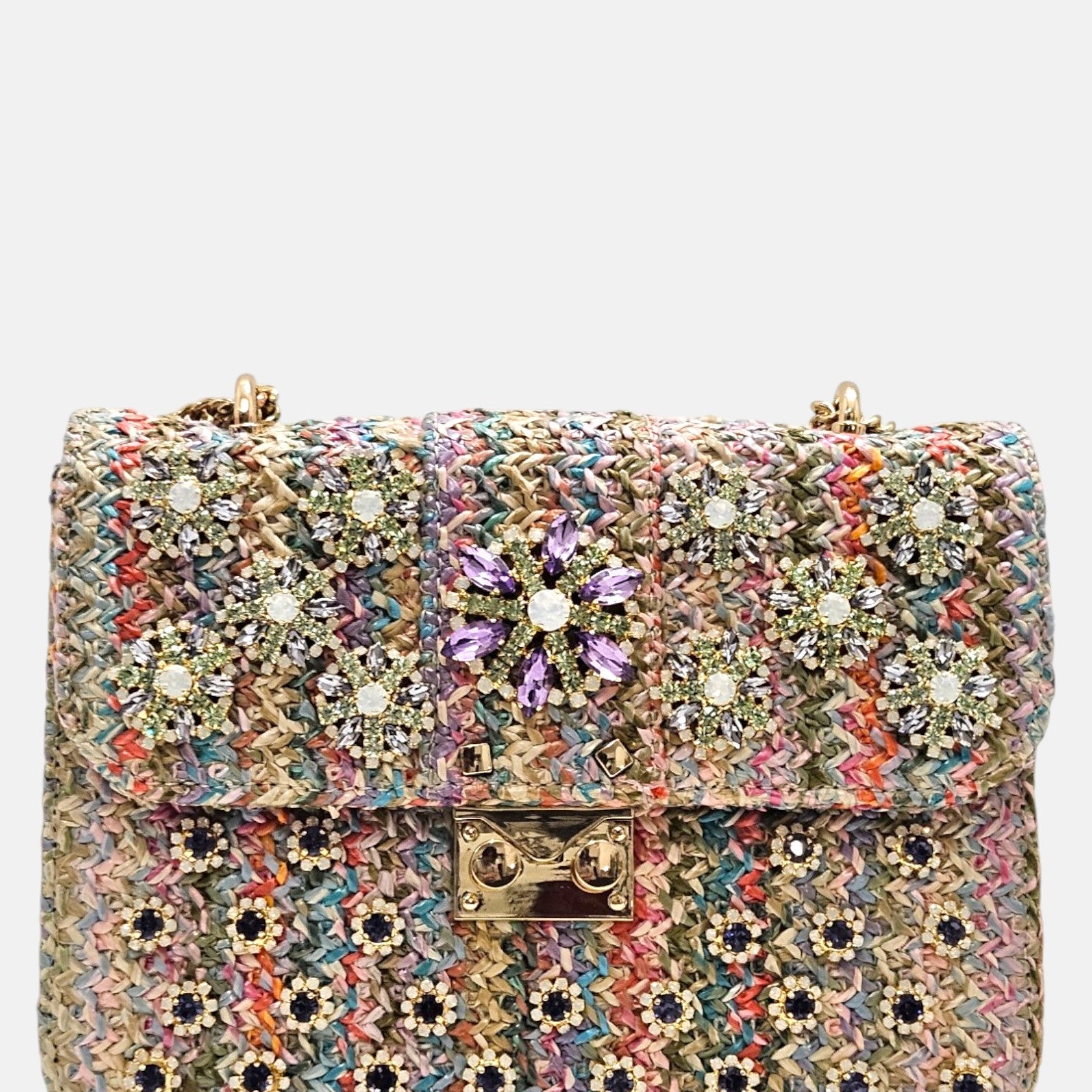 vista frontal de un bolso estructurado de Emanuela Caruso elaborado en un tejido multicolor trenzado, con una solapa decorada con flores de piedras de cristal violetas y verdes, y un broche dorado central.