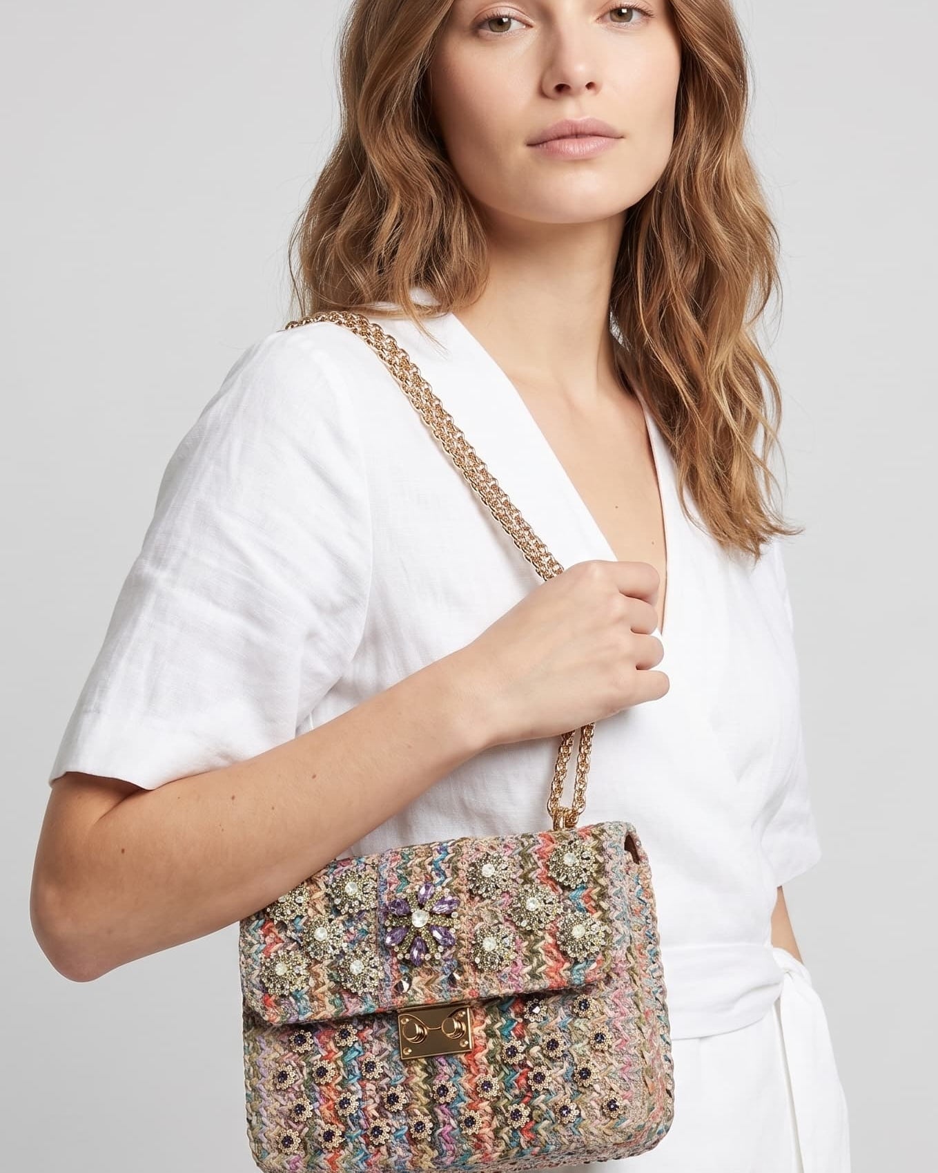 modelo de perfil con un vestido blanco cruzado mientras lleva el bolso joya de Emanuela Caruso colgado del hombro mediante su asa doble de cadena dorada.
