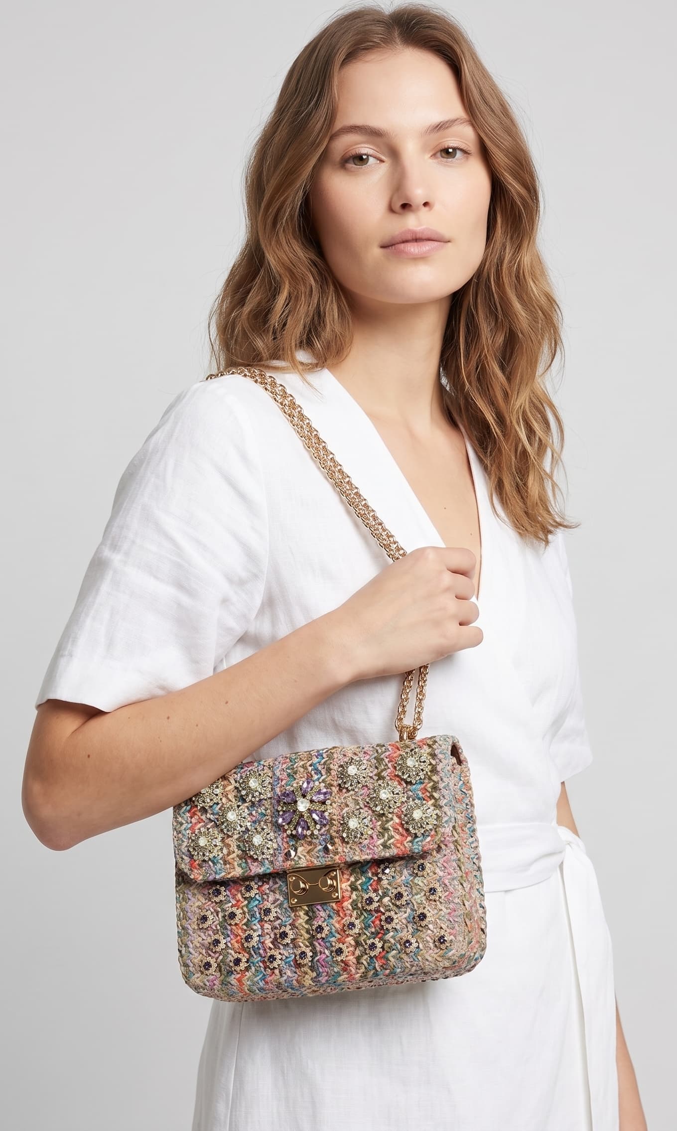modelo de perfil con un vestido blanco cruzado mientras lleva el bolso joya de Emanuela Caruso colgado del hombro mediante su asa doble de cadena dorada.
