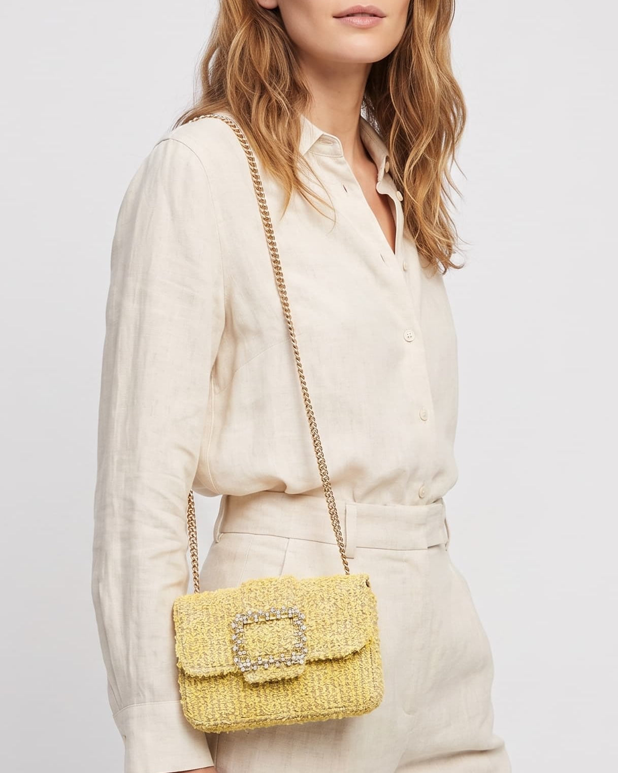 modelo luciendo una camisa de lino y un pantalón beige de perfil mientras lleva el bolso de Emanuela Caruso colgado al hombro mediante su correa de cadena dorada.