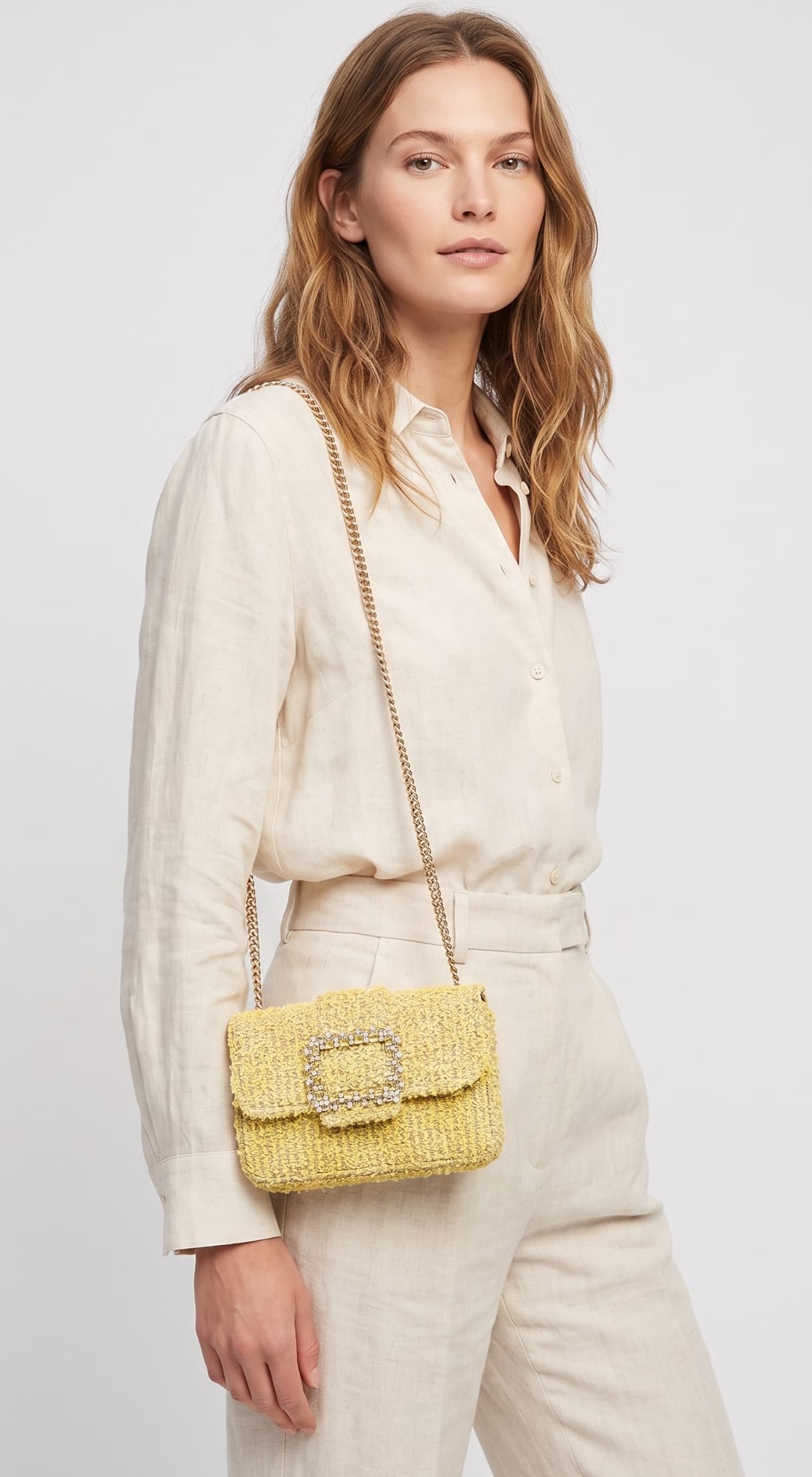 modelo luciendo una camisa de lino y un pantalón beige de perfil mientras lleva el bolso de Emanuela Caruso colgado al hombro mediante su correa de cadena dorada.
