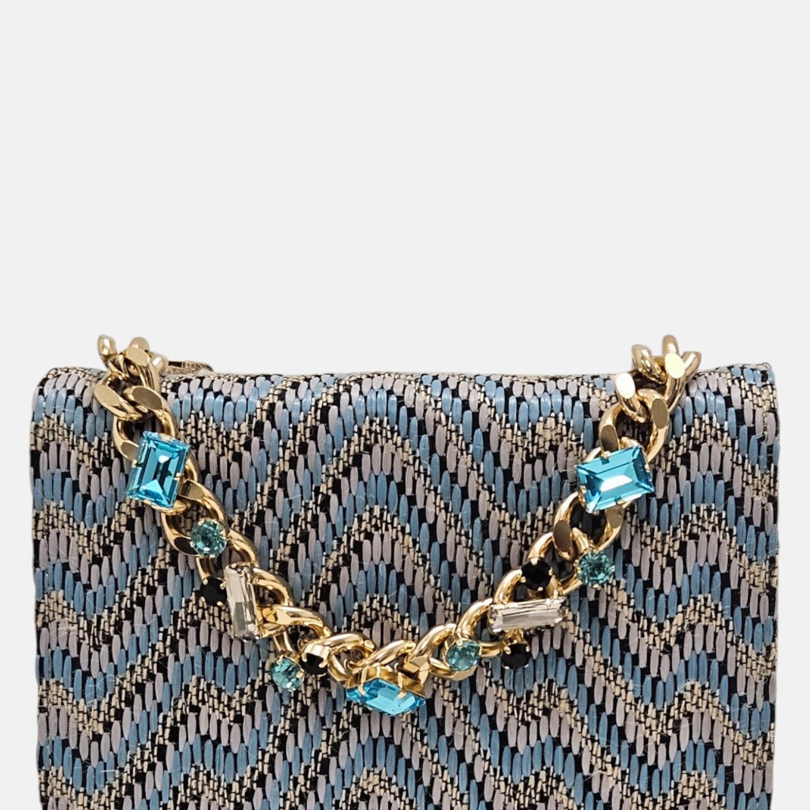 parte delantera de un bolso estructurado de Emanuela Caruso con un patrón chevron textil en tonos azules y grises, decorado con una cadena dorada engastada con piedras de cristal celestes y oscuras.
