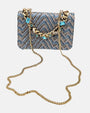 bolso textil con diseño de zig-zag de Emanuela Caruso al completo, enseñando la caída de su fina bandolera de eslabones dorados sobre un fondo claro.