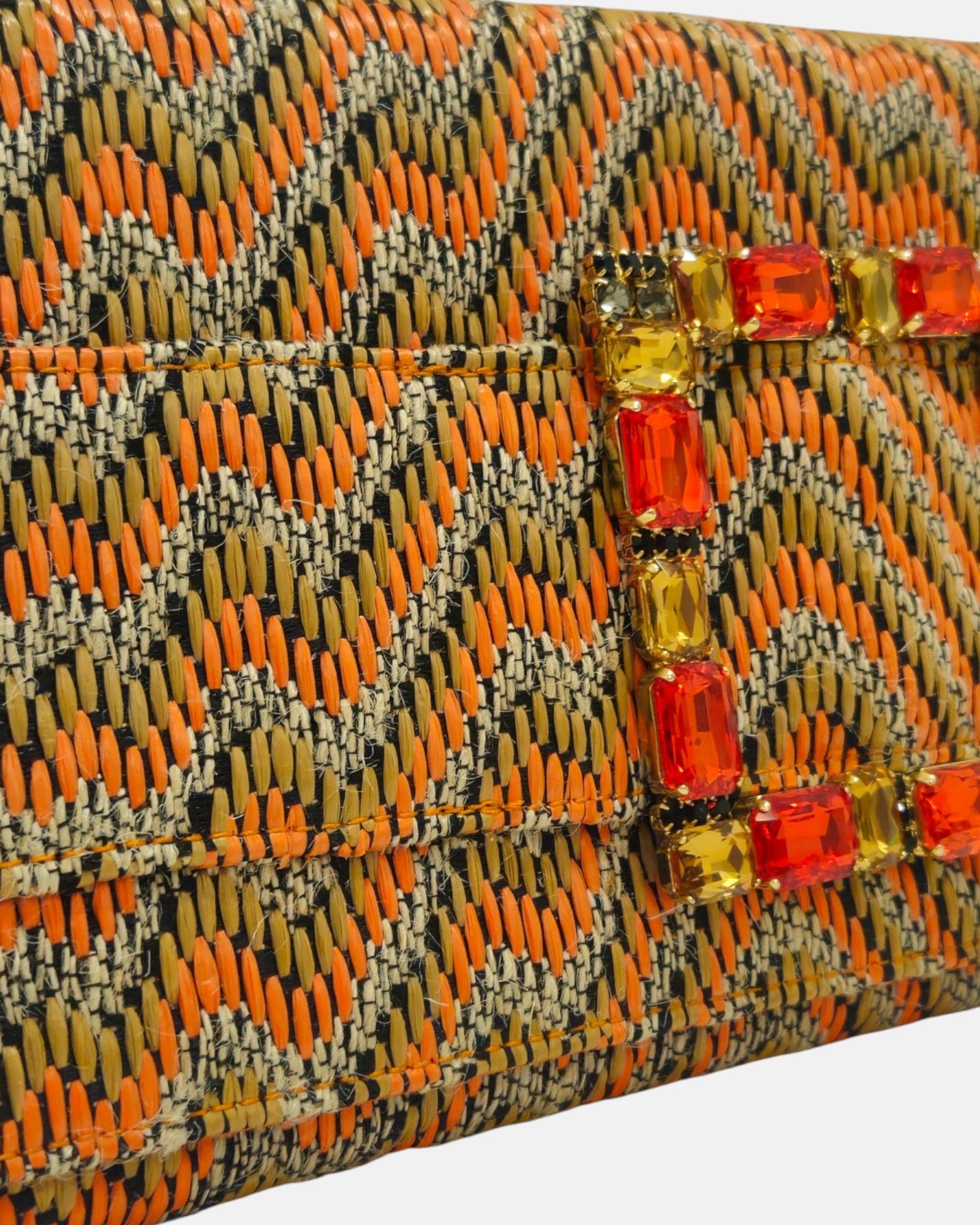primer plano macro en ángulo del broche central, resaltando el minucioso engaste de las piedras de cristal rectangulares facetadas en tonos naranjas y dorados brillantes sobre el tejido de alta calidad.