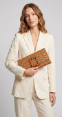 modelo posando con un traje de chaqueta blanco de lino mientras sujeta la cartera Piazzetta de Emanuela Caruso elegantemente frente al cuerpo.