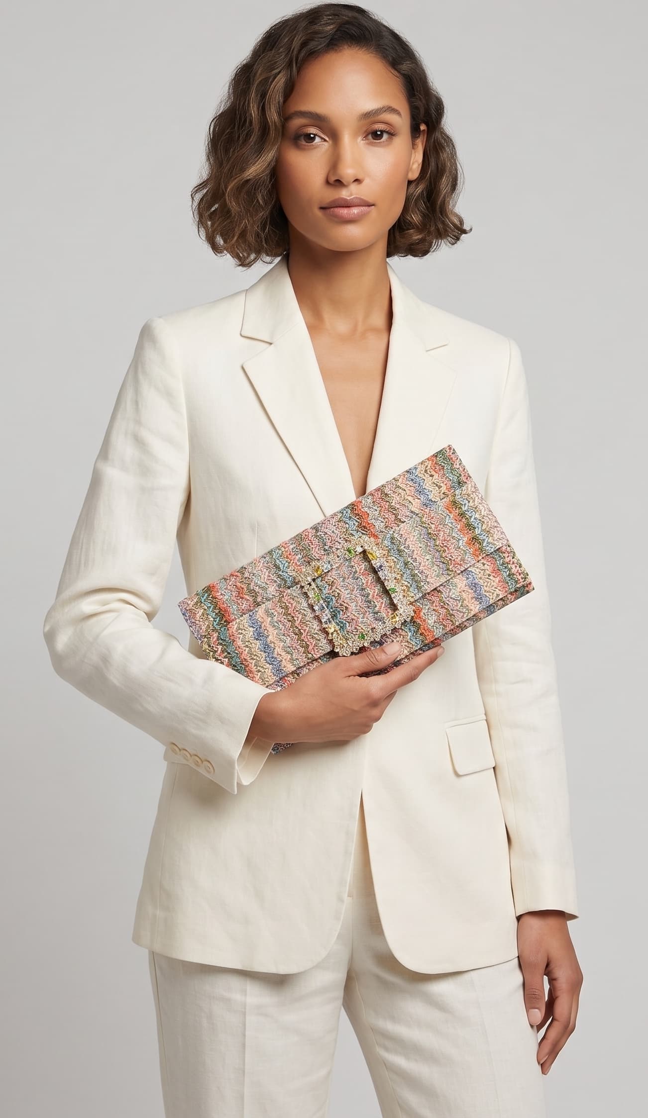 modelo posando con un traje de chaqueta blanco mientras sujeta la cartera de Emanuela Caruso con elegancia frente a ella.
