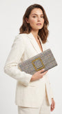 modelo posando con un traje de chaqueta blanco mientras sostiene la cartera de Emanuela Caruso con elegancia hacia un lado.