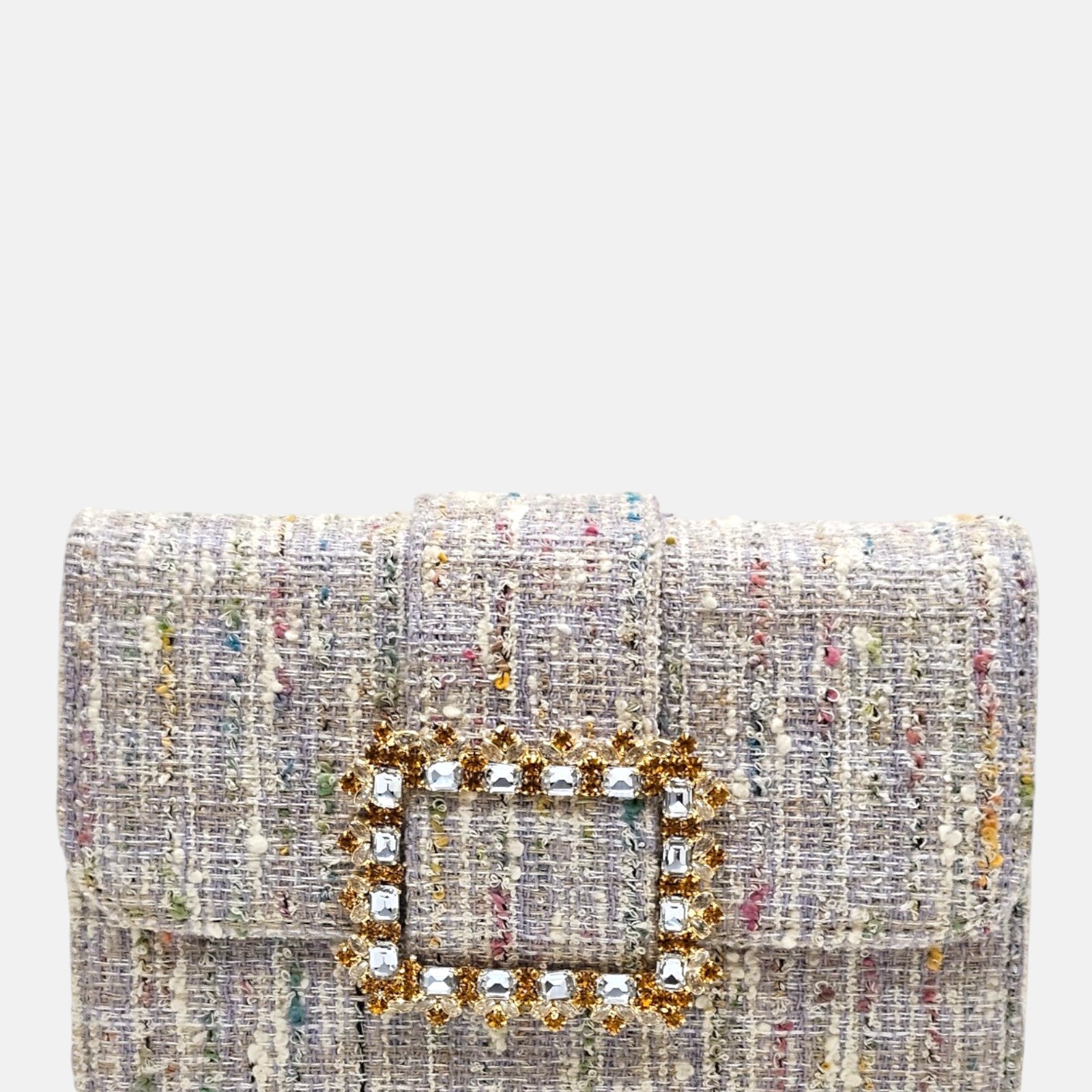 plano frontal de un bolso estructurado de Emanuela Caruso realizado en un elegante tejido jaspeado de tonos suaves, resaltando una gran hebilla dorada central recubierta de piedras de cristal claras y doradas.