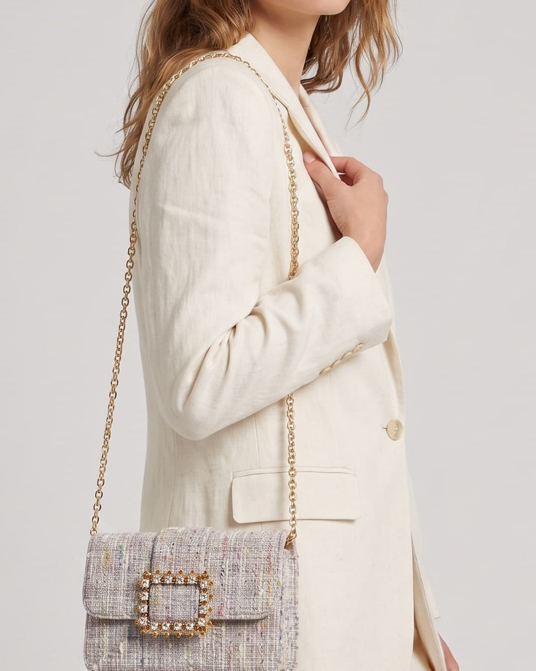 modelo de perfil luciendo una chaqueta beige mientras lleva el bolso joya de Emanuela Caruso colgado del hombro mediante su fina cadena dorada.