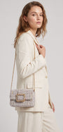 modelo de perfil luciendo una chaqueta beige mientras lleva el bolso joya de Emanuela Caruso colgado del hombro mediante su fina cadena dorada.