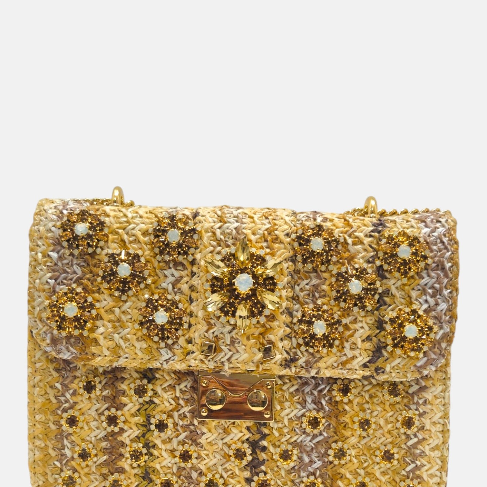 vista frontal de un bolso estructurado de Emanuela Caruso elaborado en un tejido trenzado en tonos ocre y marrón, con una solapa decorada con flores de piedras de cristal ámbar y doradas, y un broche dorado central.