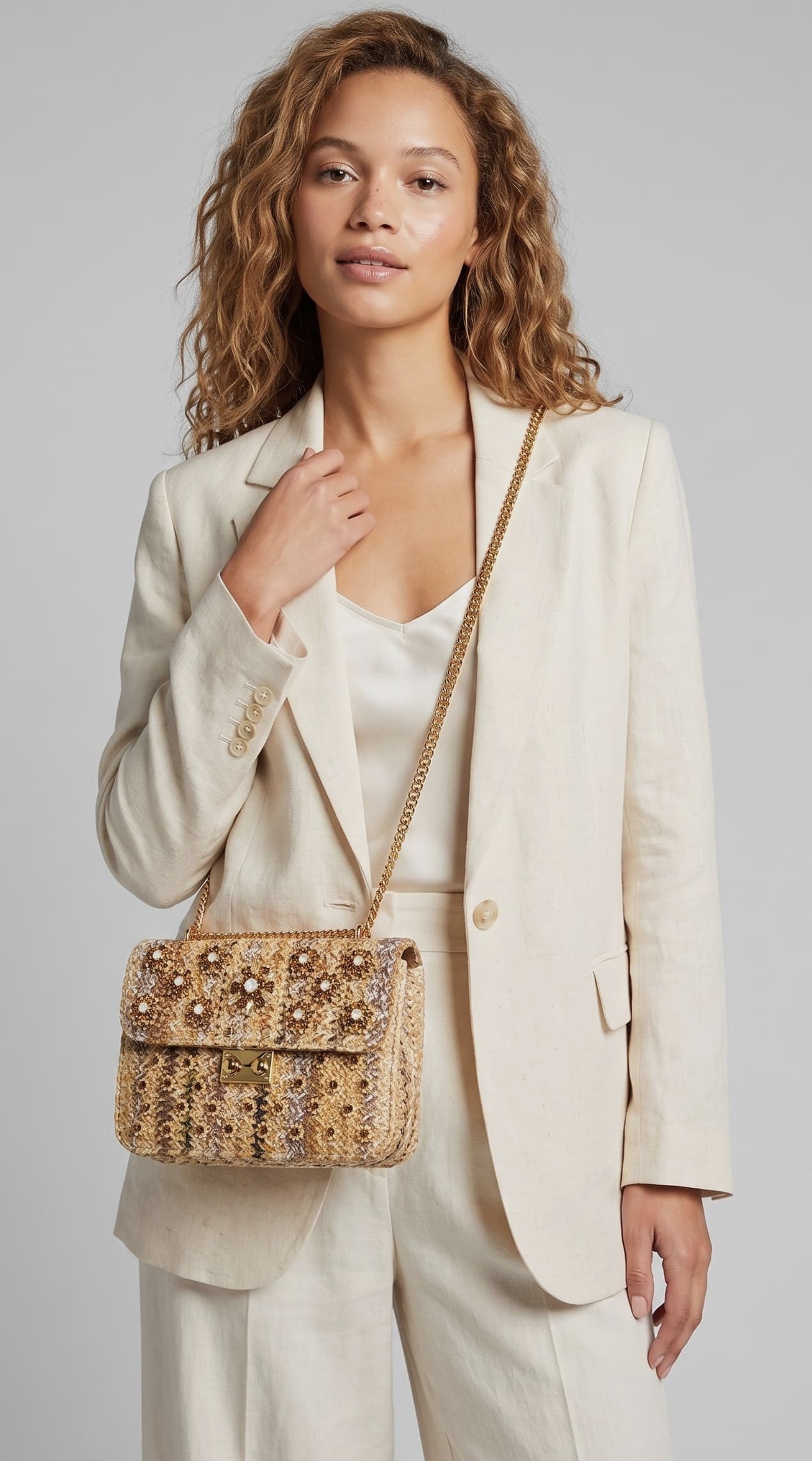 modelo con un traje de chaqueta color crema mientras lleva el bolso joya dorado de Emanuela Caruso colgado del hombro mediante su asa de cadena dorada.