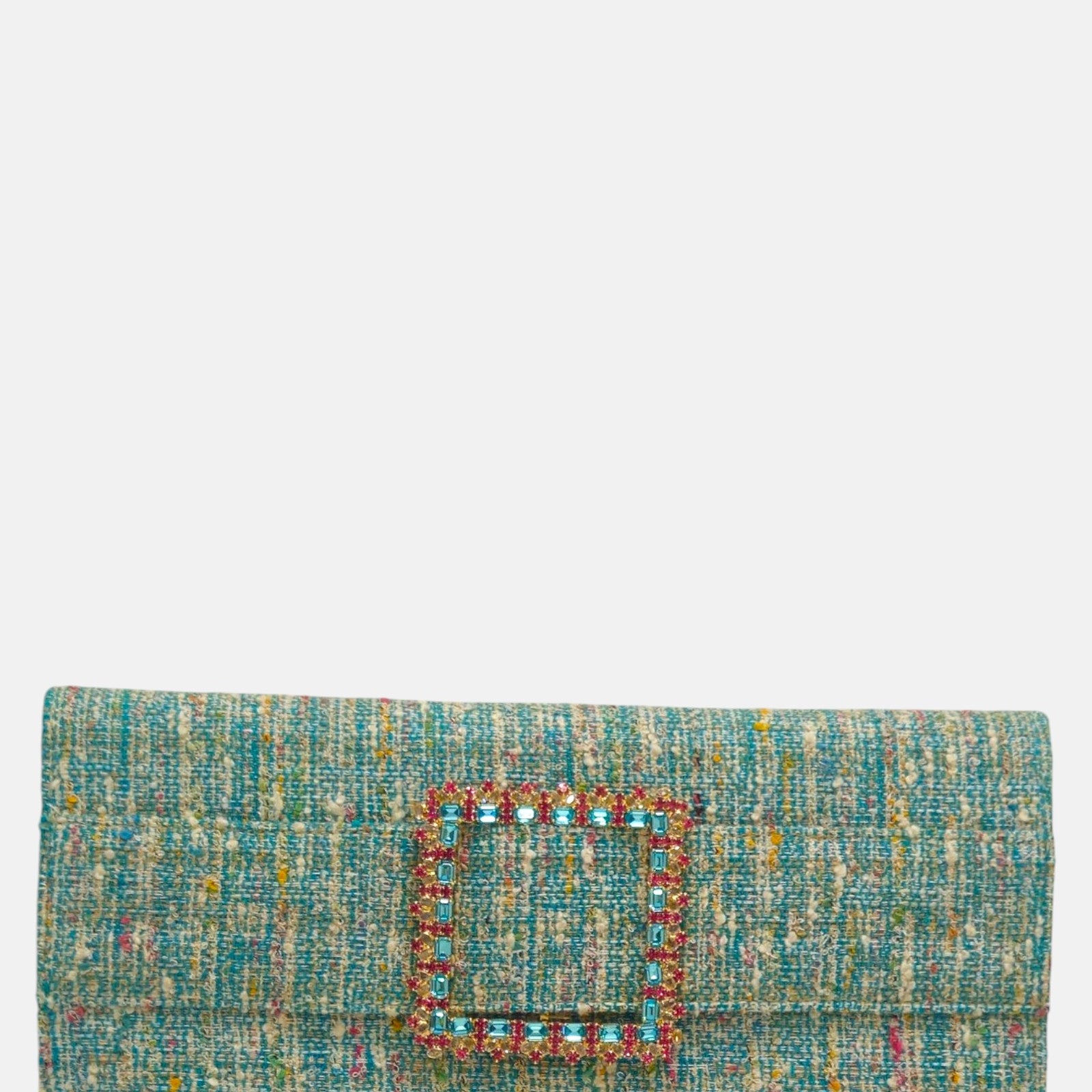vista frontal de la cartera de mano tipo sobre de Emanuela Caruso realizada en un refinado tejido jaspeado turquesa, decorada con una gran hebilla cuadrada dorada con piedras de cristal celestes y fucsias.
