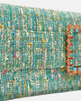 primer plano angular de la solapa, destacando la textura del tejido textil premium turquesa y el minucioso engaste de las piedras de cristal rectangulares celestes y fucsias de la hebilla.